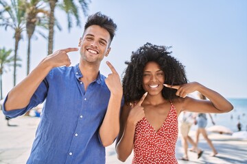 Young interracial couple outdoors on a sunny day smiling cheerful showing and pointing with fingers...