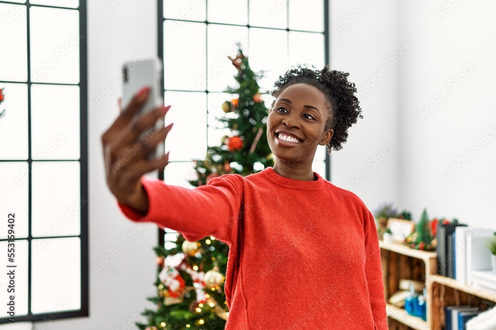 Poster African american woman make selfie by smartphone standing by christmas tree at home