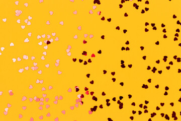 Metallic red confetti in a heart shaped scattered on a yellow background. Festive texture.