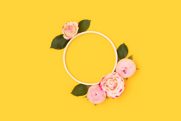 Round frame made of green leaves and pink rose flowers on a yellow background. Place for text.