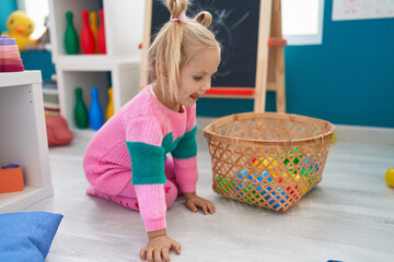 Adorable caucasian girl playing with balls sitting on floor at kindergarten