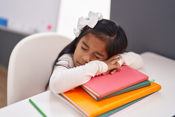 Adorable hispanic girl student leaning on book sleeping at classroom