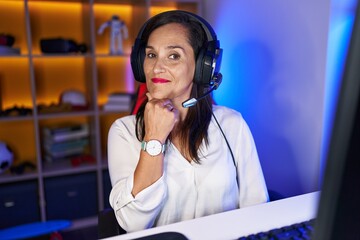 Middle age brunette woman playing video games smiling looking confident at the camera with crossed arms and hand on chin. thinking positive. © Krakenimages.com