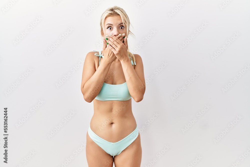 Poster young caucasian woman wearing bikini over isolated background shocked covering mouth with hands for 