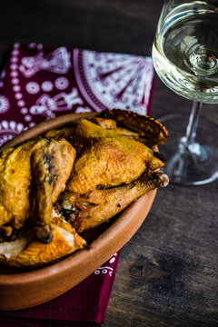 Dish with chicken tabaka and a glass of white wine on a table with a traditional tablecloth