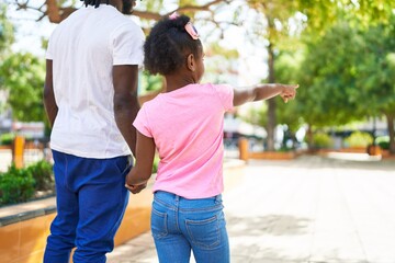 Father and daughter walking with hands together pointing with finger at park