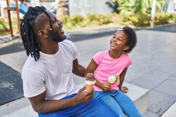 Father and daughter eating ice cream sitting together on bench at park
