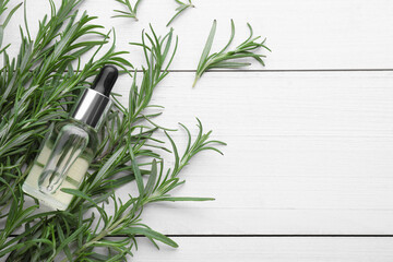 Fresh green rosemary and bottle of essential oil on white wooden table, flat lay. Space for text