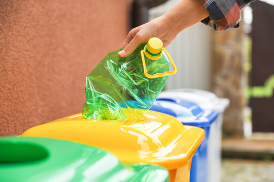 Woman throwing plastic bottle into recycling bin outdoors, closeup