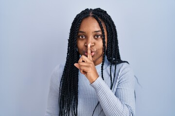 Fototapeta na wymiar African american woman standing over blue background asking to be quiet with finger on lips. silence and secret concept.