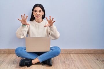 Young woman using laptop sitting on the floor at home smiling funny doing claw gesture as cat,...