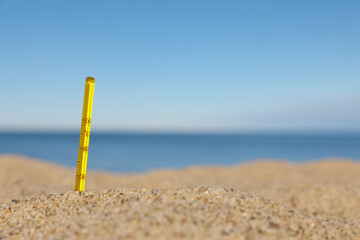 Weather thermometer in sand near sea, space for text
