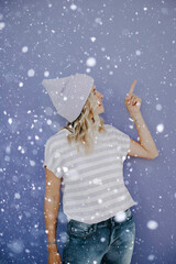 beautiful woman stands in snowfall with beanie and ripened shirt is standing in front of purple background