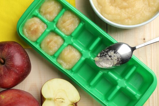 Apple puree in ice cube tray with fresh apple fruits on wooden table, flat lay. Ready for freezing