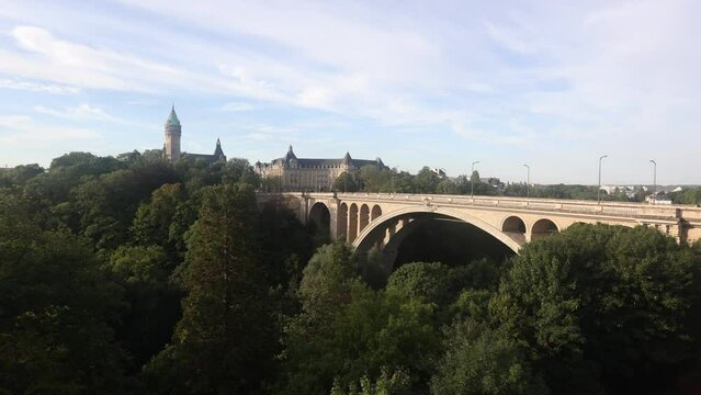 Scenic view of Adolphe Bridge, stone arched aqueduct running over green valley of Petrusse River in Luxembourg city with State Savings Bank and banking museum in background on sunny summer day. High