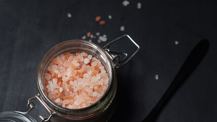 Pink Himalayan salt crystals in a glass jar on a dark background
