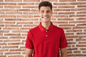 Young hispanic man standing over bricks wall with a happy and cool smile on face. lucky person.