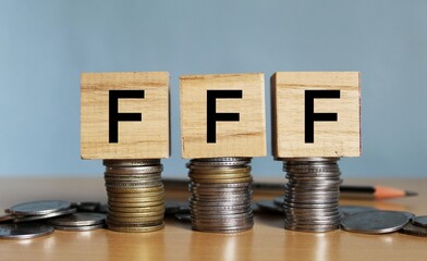 FFF (Friends, Family, Fools) - word on wooden blocks with stacked coins, FFF concept. 