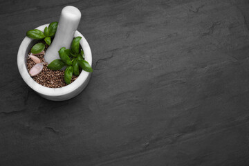 Mortar with peppercorns, basil and garlic on black table, above view. Space for text