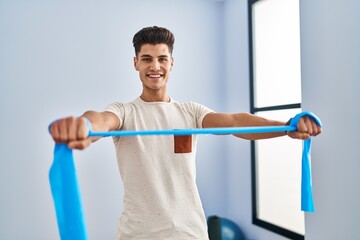 Fototapeta na wymiar Young hispanic man smiling confident training using elastic band at sport center