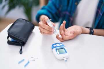 Young hispanic man measuring glucose sitting on table at home