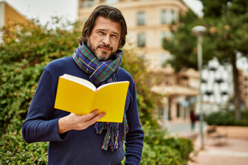 Middle age handsome man reading a book outdoors at the park