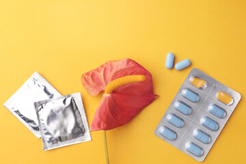 Anthurium flower symbolizing male sexual organ, pills and condoms on orange background, flat lay....