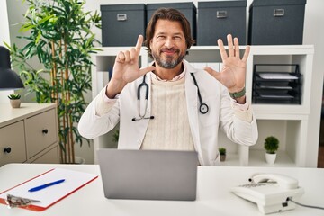 Handsome middle age doctor man working at the clinic showing and pointing up with fingers number...