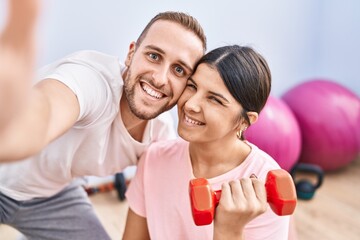 Man and woman couple training using dumbbells make selfie by the camera at sport center