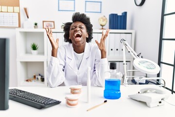 African dentist woman working at medical clinic celebrating mad and crazy for success with arms raised and closed eyes screaming excited. winner concept