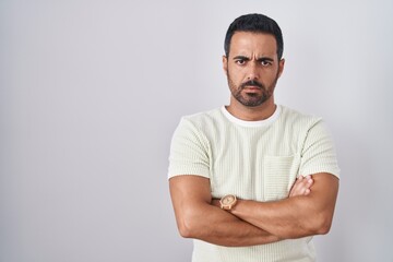 Fototapeta premium Hispanic man with beard standing over isolated background skeptic and nervous, disapproving expression on face with crossed arms. negative person.