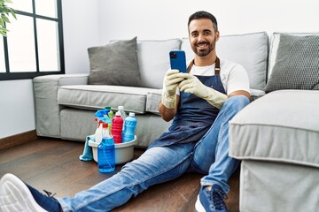 Young hispanic man wearing apron and gloves using smartphone at home