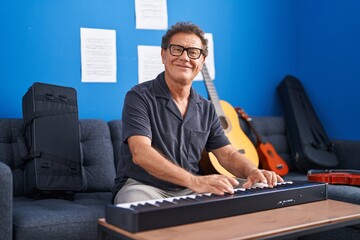 Middle age man musician smiling confident playing piano at music studio