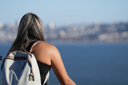 the girl with the backpack on her back looks towards the sea. photo during the day.
