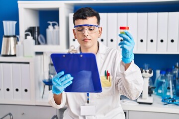 Young non binary man scientist reading report holding urine test tube at laboratory