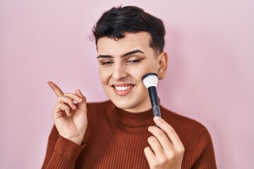 Non binary person applying make up smiling happy pointing with hand and finger to the side