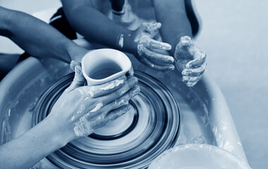 Potter teaching child to make ceramic pot on the pottery wheel