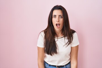 Obraz premium Young brunette woman standing over pink background afraid and shocked with surprise and amazed expression, fear and excited face.