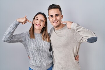 Young hispanic couple standing over white background smiling cheerful showing and pointing with fingers teeth and mouth. dental health concept.