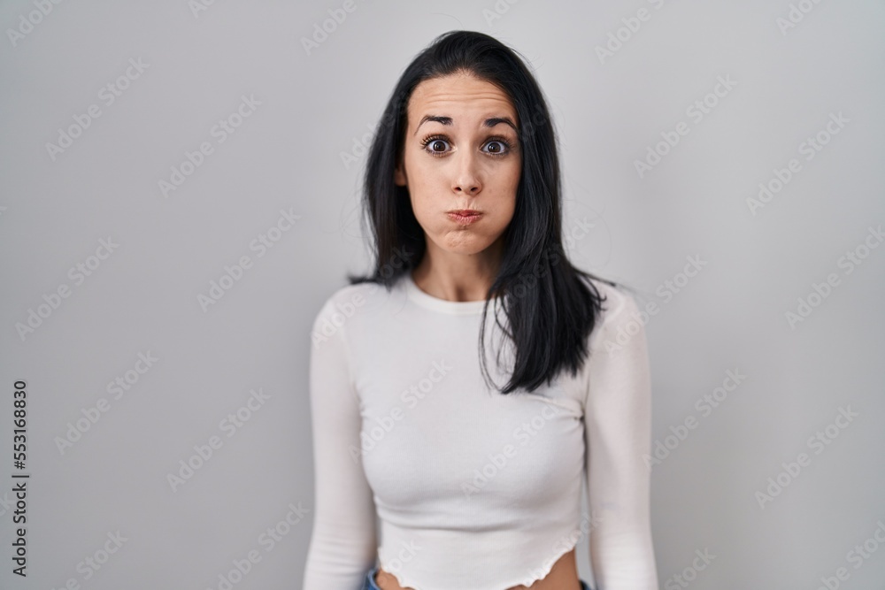 Sticker Hispanic woman standing over isolated background puffing cheeks with funny face. mouth inflated with air, crazy expression.