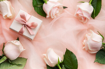Top view of pink roses and gift box on pink tulle background.