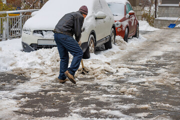 A man removes snow and ice stuck to the road with a shovel from the sidewalk.