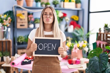 Young blonde woman working at florist holding open sign looking at the camera blowing a kiss being lovely and sexy. love expression.