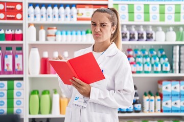 Young blonde woman working at pharmacy drugstore holding notebook skeptic and nervous, frowning upset because of problem. negative person.