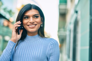 Young hispanic woman speaking on the phone at the town