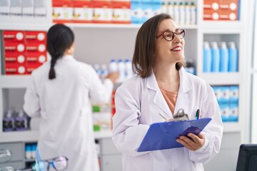Two women pharmacist smiling confident writing on document at pharmacy