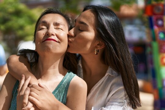 Two women mother and daughter hugging each other kissing at park