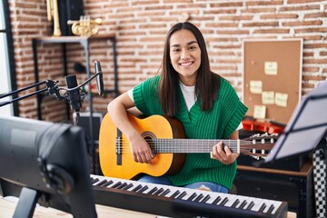 Fototapeta na wymiar Young hispanic woman musician playing classical guitar at music studio