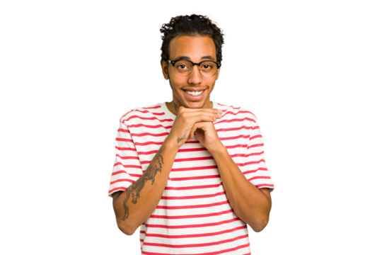 Young African American man isolated keeps hands under chin, is looking happily aside.