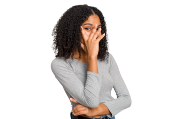 Young african american woman with curly hair cut out isolated blink at the camera through fingers, embarrassed covering face.